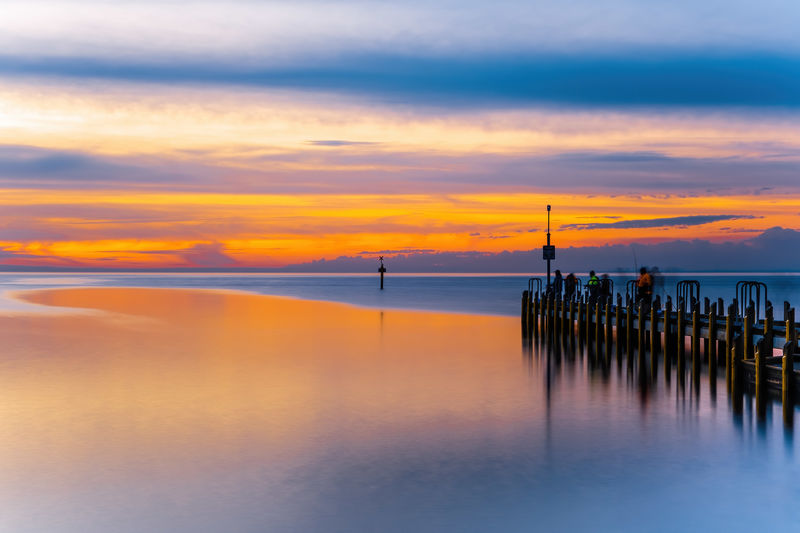 Vivid glowing orange sunset over ocean and boat jetty - long exposure seascape