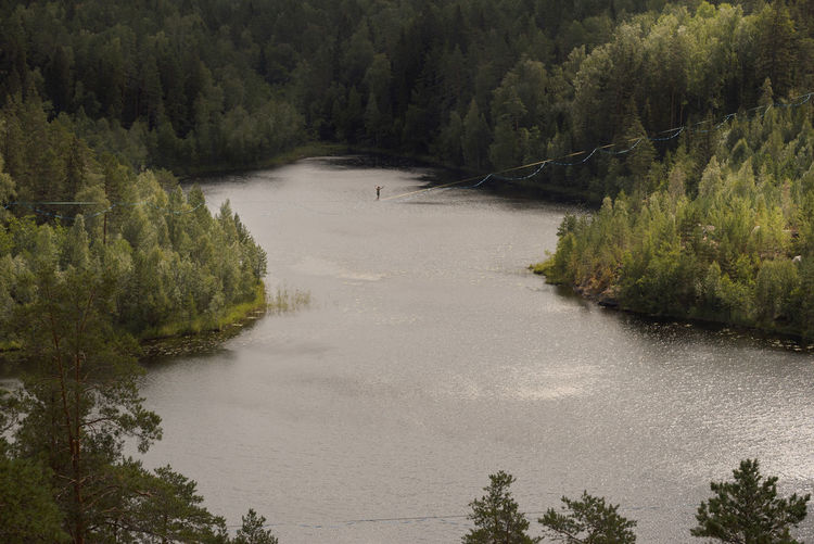 A tightrope walker on a slackline over a picturesque forest lake. extreme sports theme