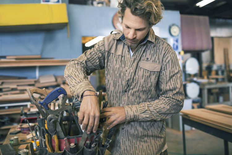 Carpenter arranging tools in belt at workshop