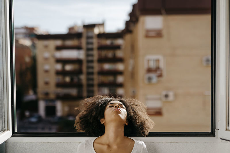 Young woman resting head on window sill at home