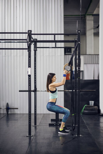 Side view of female athlete exercising with gymnastic rings in health club