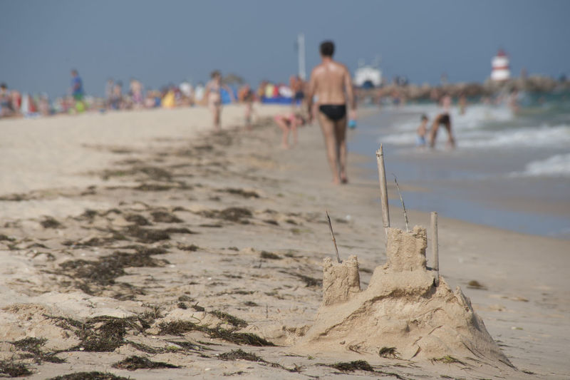 Sandcastle with shirtless man walking at beach