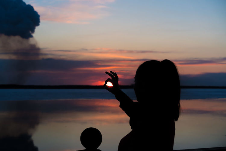 Silhouette woman showing ok sign against sky during sunset