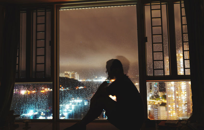 Rear view of woman looking through window at night