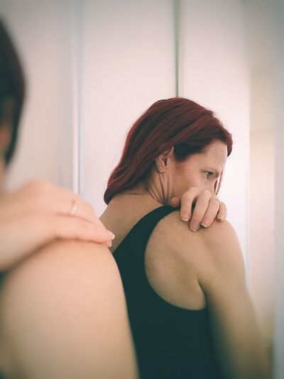 Woman scratching shoulder while reflecting on mirror at home