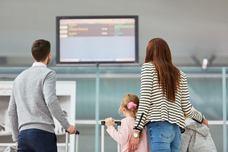 Rear view of family looking at arrival departure board in airport
