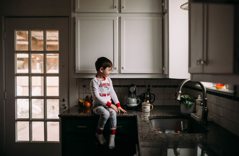 Boy sitting on kitchen counter helping make coffee for breakfast