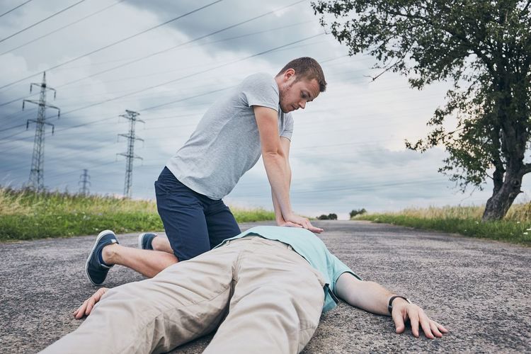 Young man giving cpr to friend lying unconscious on road