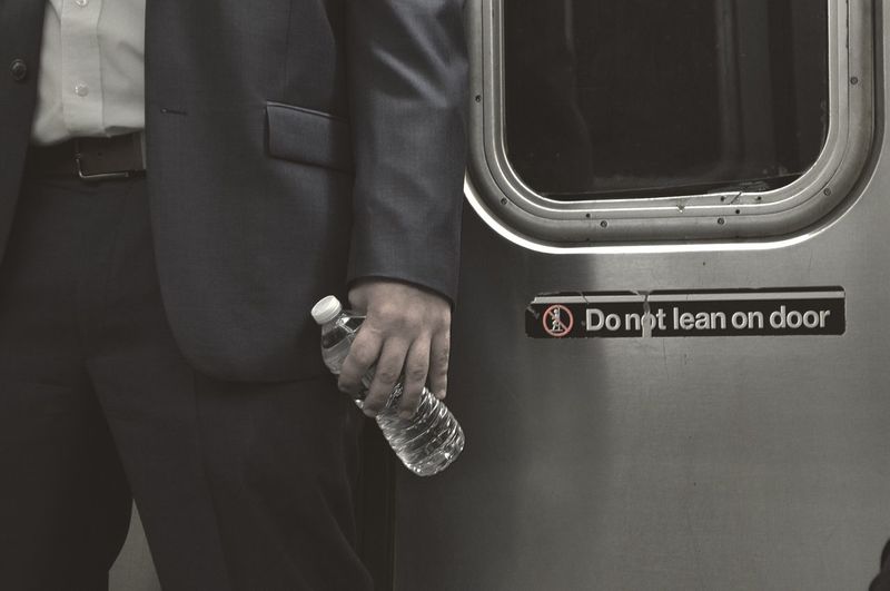Midsection of businessman standing by door in train