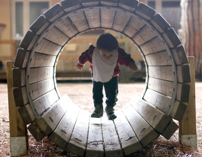 Full length of boy walking through wooden pipe at playground