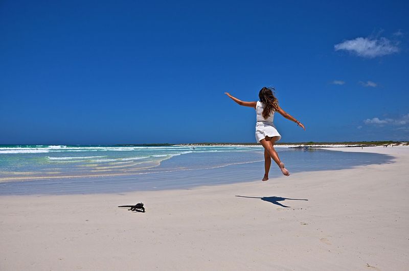 Full length of woman jumping on beach against blue sky
