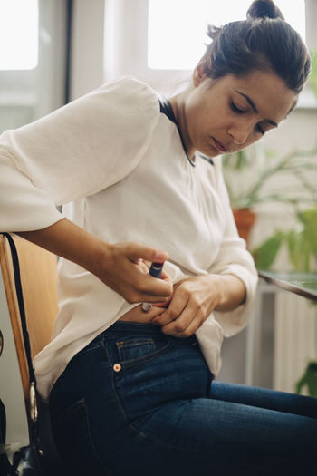 Businesswoman injecting insulin in abdomen while sitting on chair in office