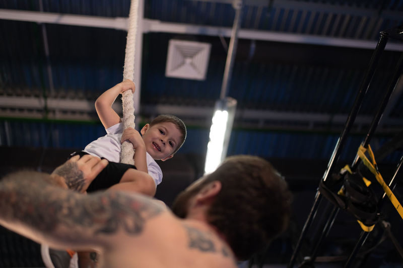 Father teaching happy boy to climb rope in gym