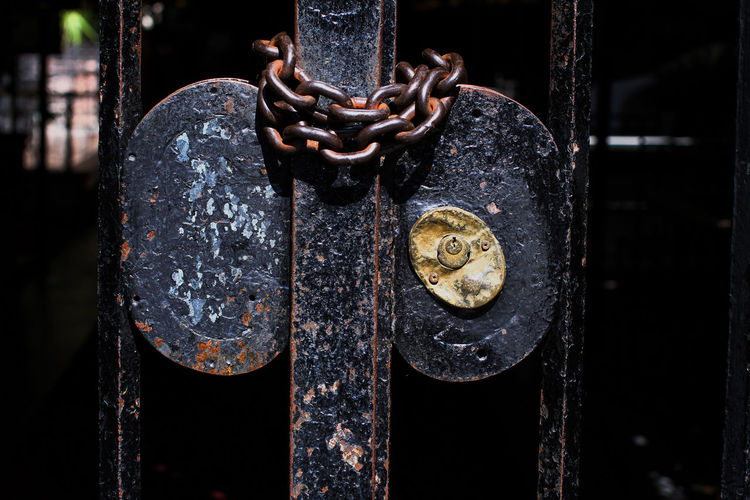 Detail of brass lock and chain of a partially rusted iron gate, dark background.