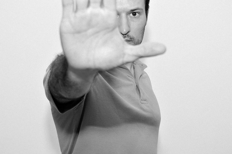 Portrait of man gesturing stop sign while standing against white background