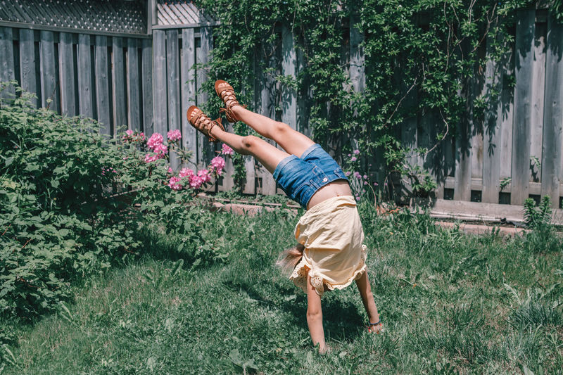 Girl balancing on handstand at yard against fence