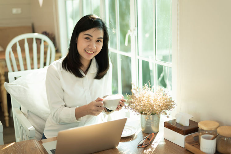 Portrait of smiling young woman using phone at home