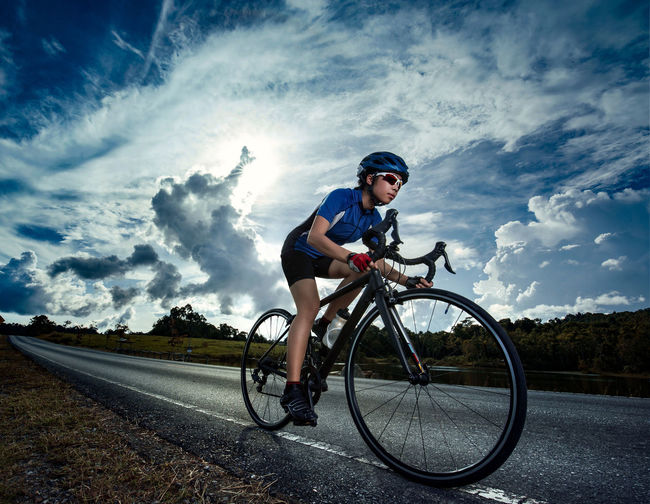 Man riding bicycle on road against cloudy sky