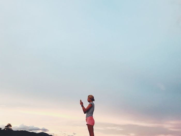 Side view of woman standing against cloudy sky during sunset