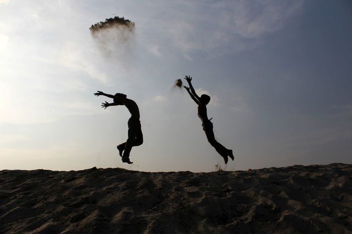 Silhouette boys jumping at beach against sky during sunset