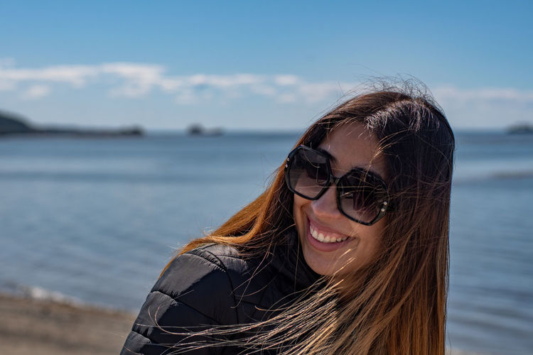 Smiling young woman wearing sunglasses against sea