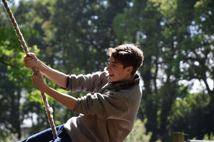 Side view of man on swing against trees at park