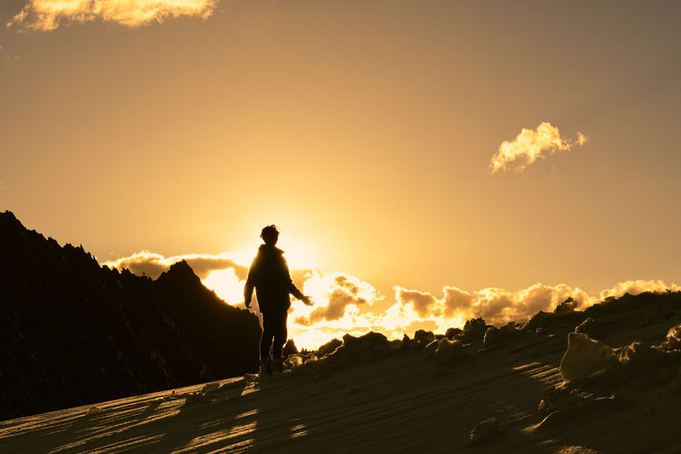Rear view of people walking on road against sky during sunset
