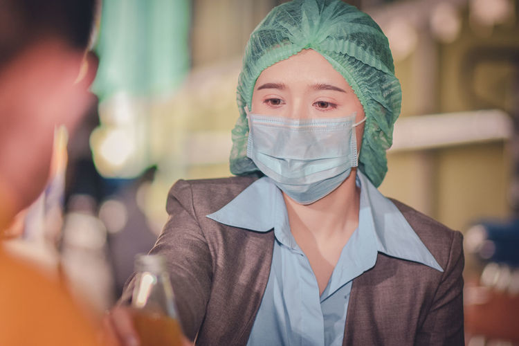 Close-up of woman wearing mask inspecting drink in factory