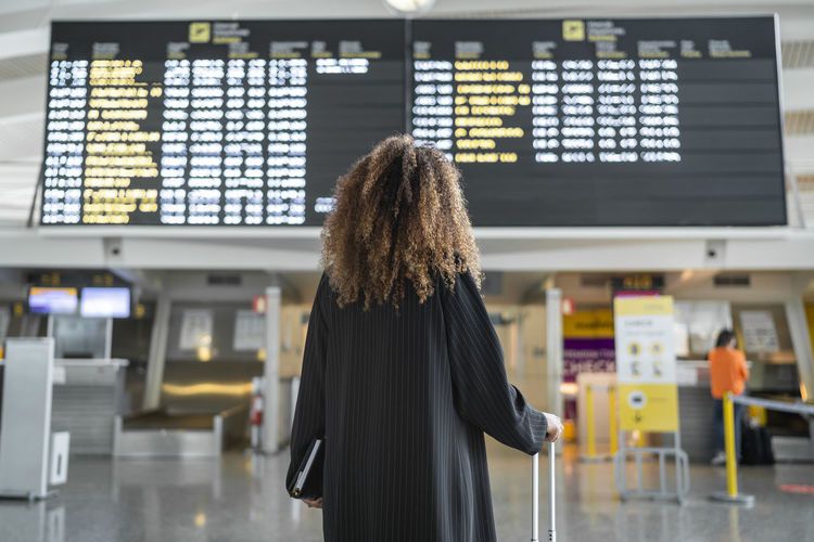 Young woman checking arrival timing of flight on board standing at airport