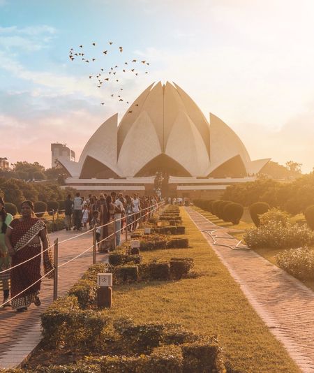 Tourists visiting lotus temple against sky during sunset