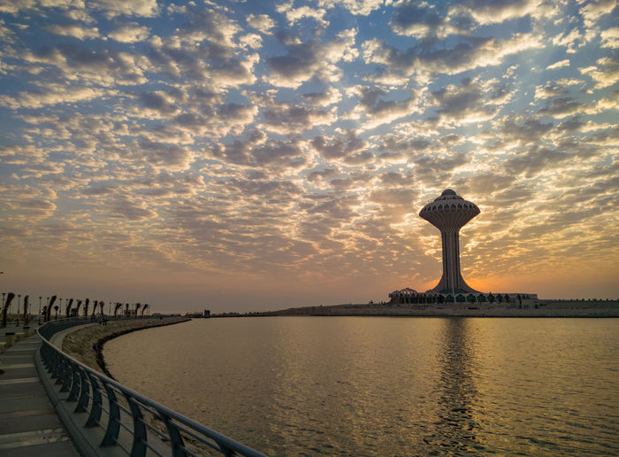 Walkway and tower by sea against sky during sunset
