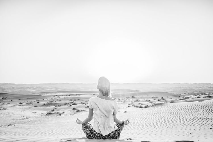 Rear view of woman meditating in desert