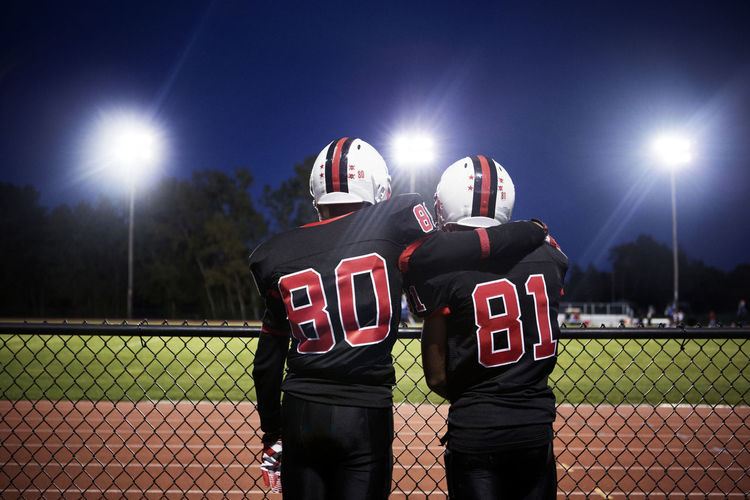 Rear view of american football players standing against illuminated field