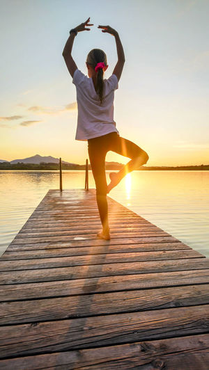 Rear view of woman dancing on pier over lake during sunset