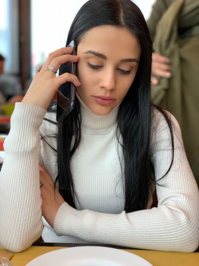 Close-up of young woman talking over mobile phone while sitting in restaurant