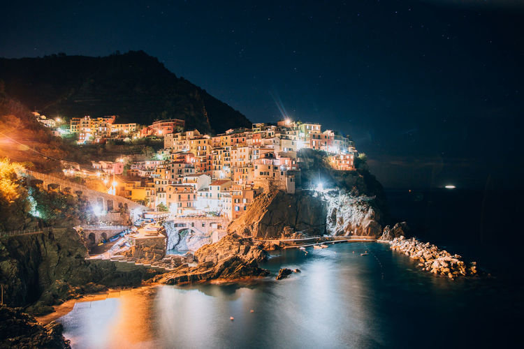 Illuminated houses on cliff by sea at night