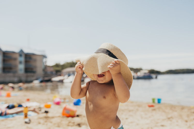 Toddler boy playing peek-a-boo with sun hat on beach