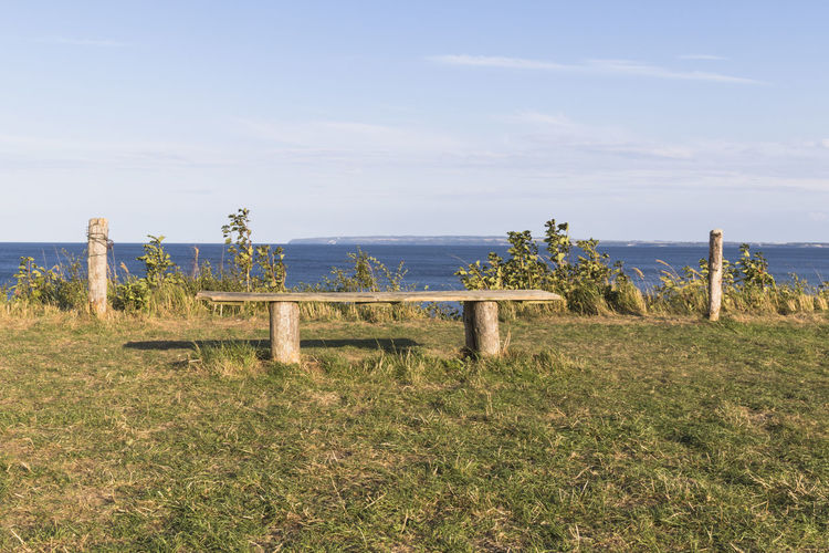 Wooden posts on field by sea against sky