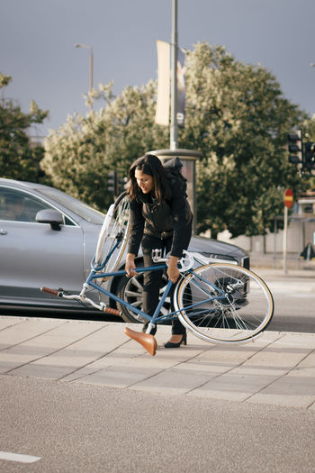 Businesswoman holding bicycle while crossing street in city