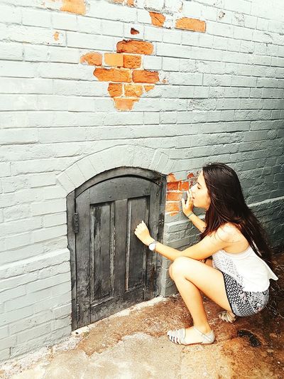 High angle view of woman crouching by small door on brick wall