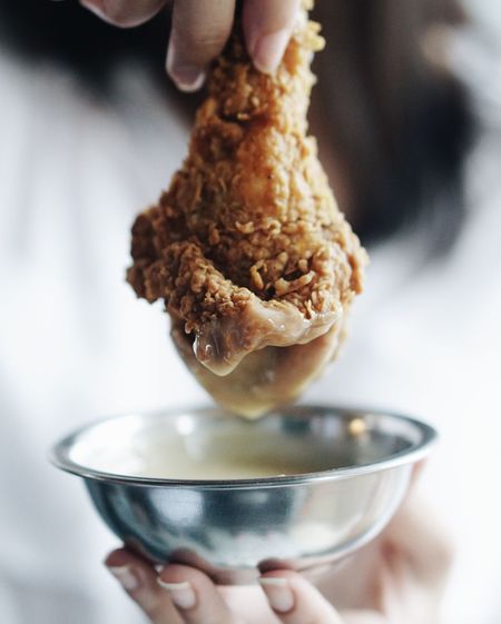 Cropped hand holding chicken wing and bowl