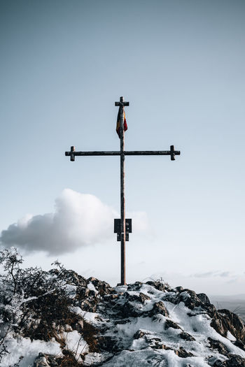 Low angle view of cross on snow covered land against sky