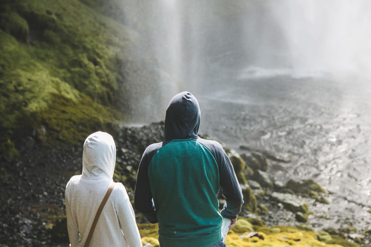 Rear view of man and woman standing against waterfall