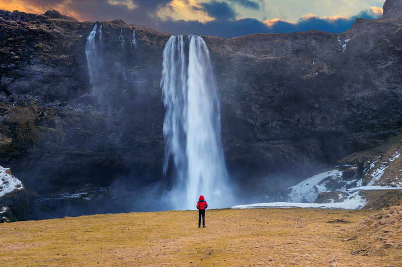 Rear view of man looking at waterfall falling from mountain