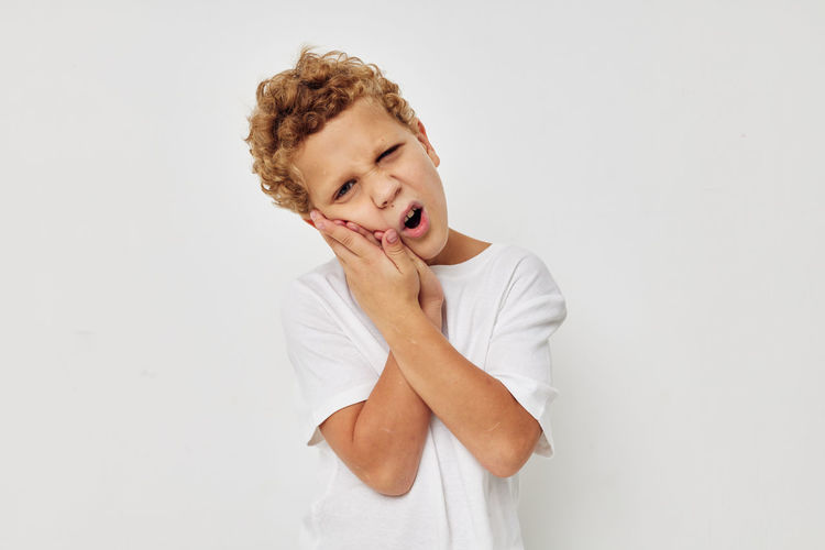 Portrait of boy having toothache against white background