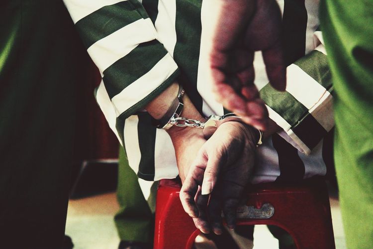 Rear view of criminal hands trapped in handcuffs