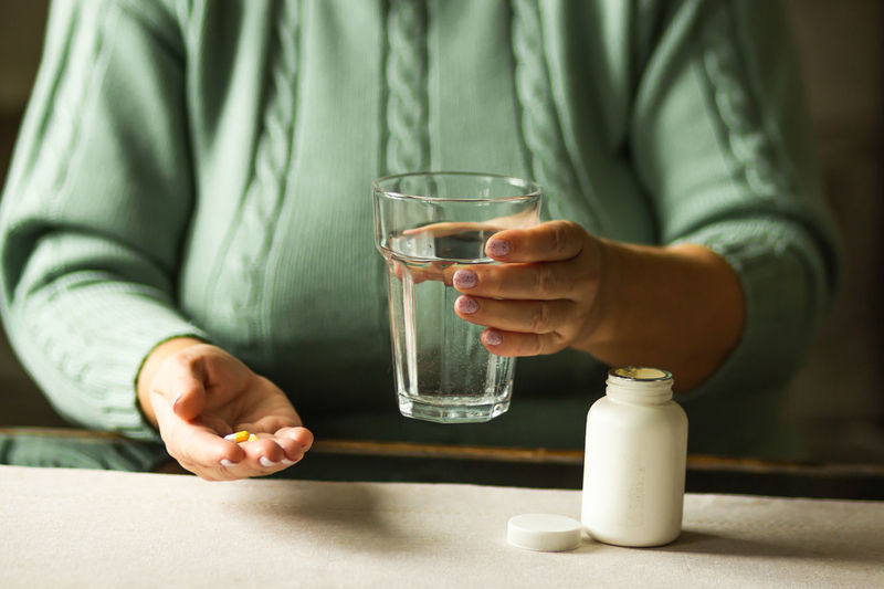 Woman's hands holds two capsules and glass of water over the table, ready to take medicines.
