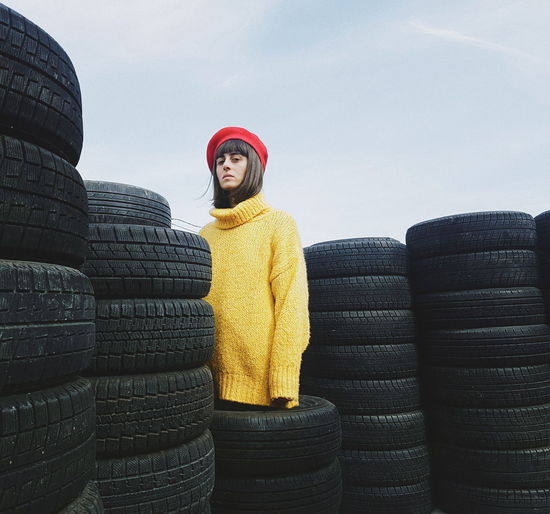 Portrait of woman standing by stacked tires against sky