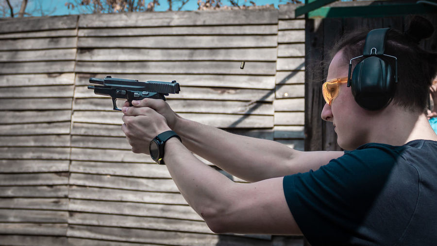 Man wearing glasses holding gun while standing outdoors