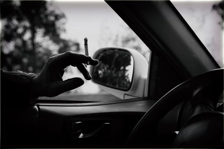 Cropped image of hand holding cigarette in car